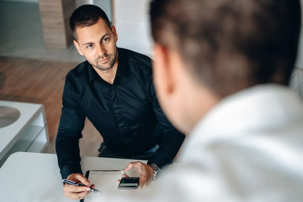 A consultant with a notepad and calculator listening to a client across a desk